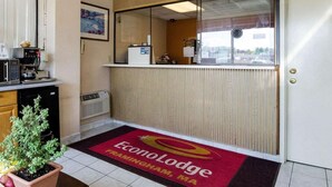 Zona de recepción con mostrador, máquina de café, planta en maceta y alfombra roja con el logotipo de Econolodge.