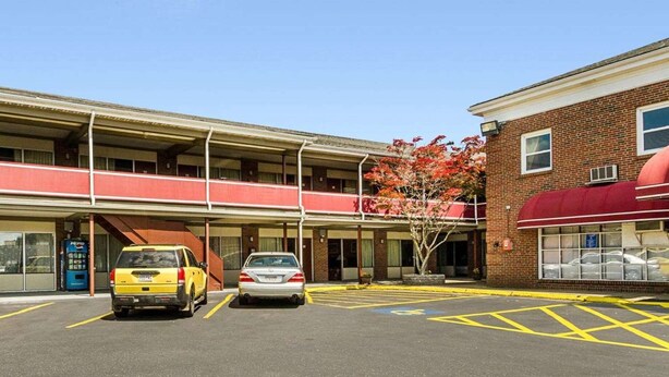 Un estacionamiento con dos autos, un edificio con toldo rojo y un cielo azul despejado.