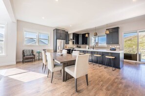 A modern kitchen with dark cabinetry, a central island with bar stools, and a dining area with a wooden table and chairs. - 12829 North Belaview Way (Daniel)