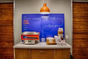 A breakfast station with a blue sign, a pancake maker, and a coffee machine.