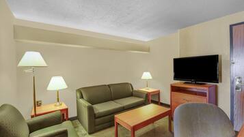 A hotel room with a green sofa, two armchairs, a wooden coffee table, a television on a wooden stand, and two lamps on side tables.