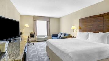 A hotel room with a bed, a desk with a flat-screen TV, a chair, a sofa, and a large window.