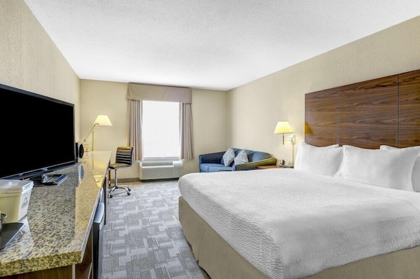A hotel room with a bed, a desk with a flat-screen TV, a chair, a sofa, and a large window. - Days Inn Red Deer (Red Deer)
