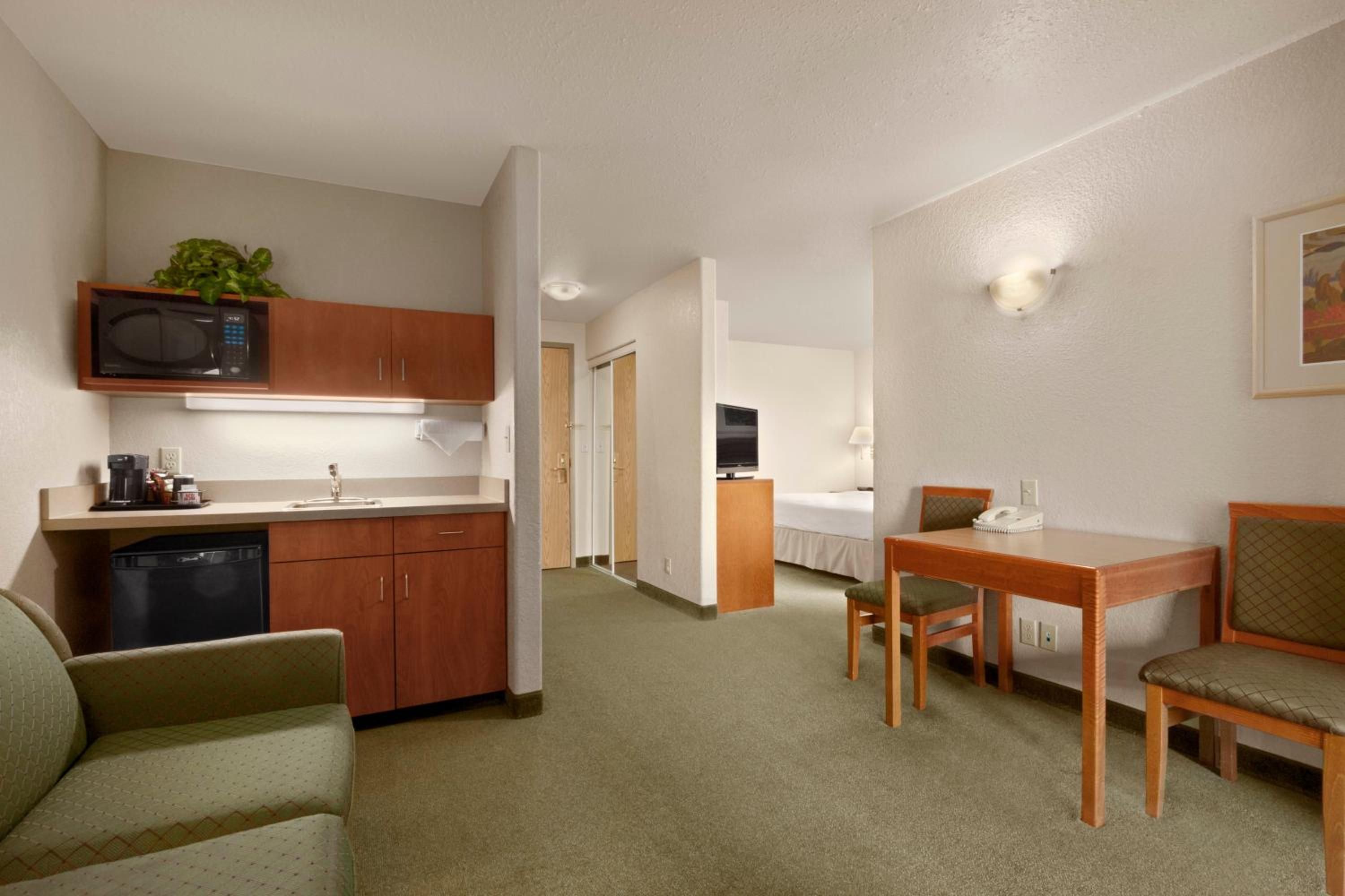 A compact hotel room with a kitchenette, a dining area, and a bed.