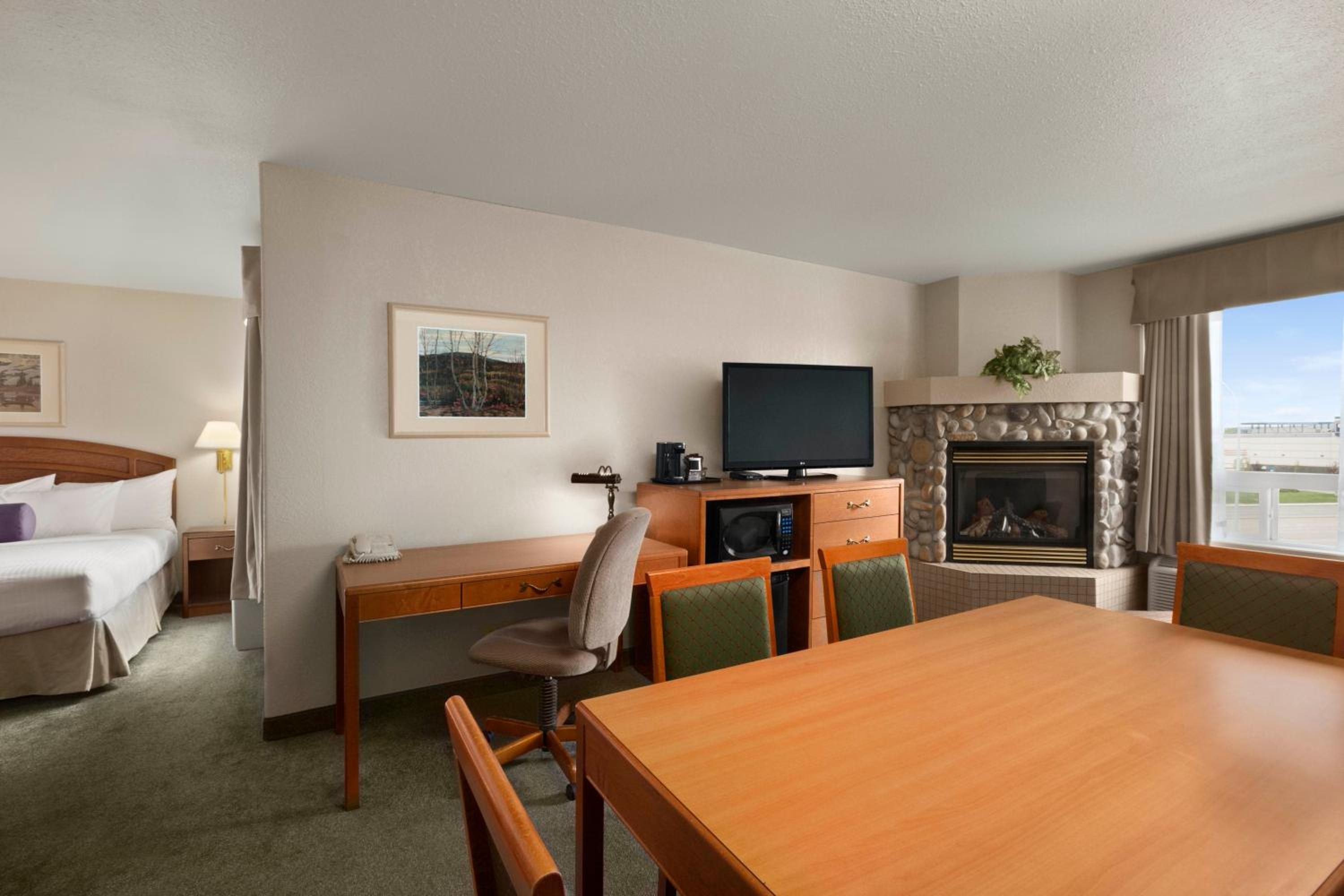 A hotel room with a bed, a desk with a television, a fireplace, and a dining table.