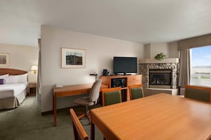 A hotel room with a bed, a desk with a television, a fireplace, and a dining table. - Days Inn Red Deer (Red Deer)