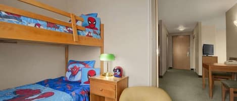 A hotel room with a bunk bed, a desk, a chair, and a television.