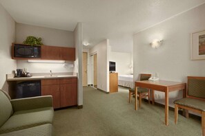 A compact hotel room with a kitchenette, a dining area, a single bed, and a small seating area.