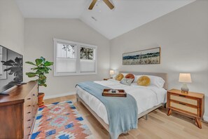 Une chambre à coucher comprenant un lit, une table de chevet, une lampe, une plante en pot, une œuvre d’art et une fenêtre.