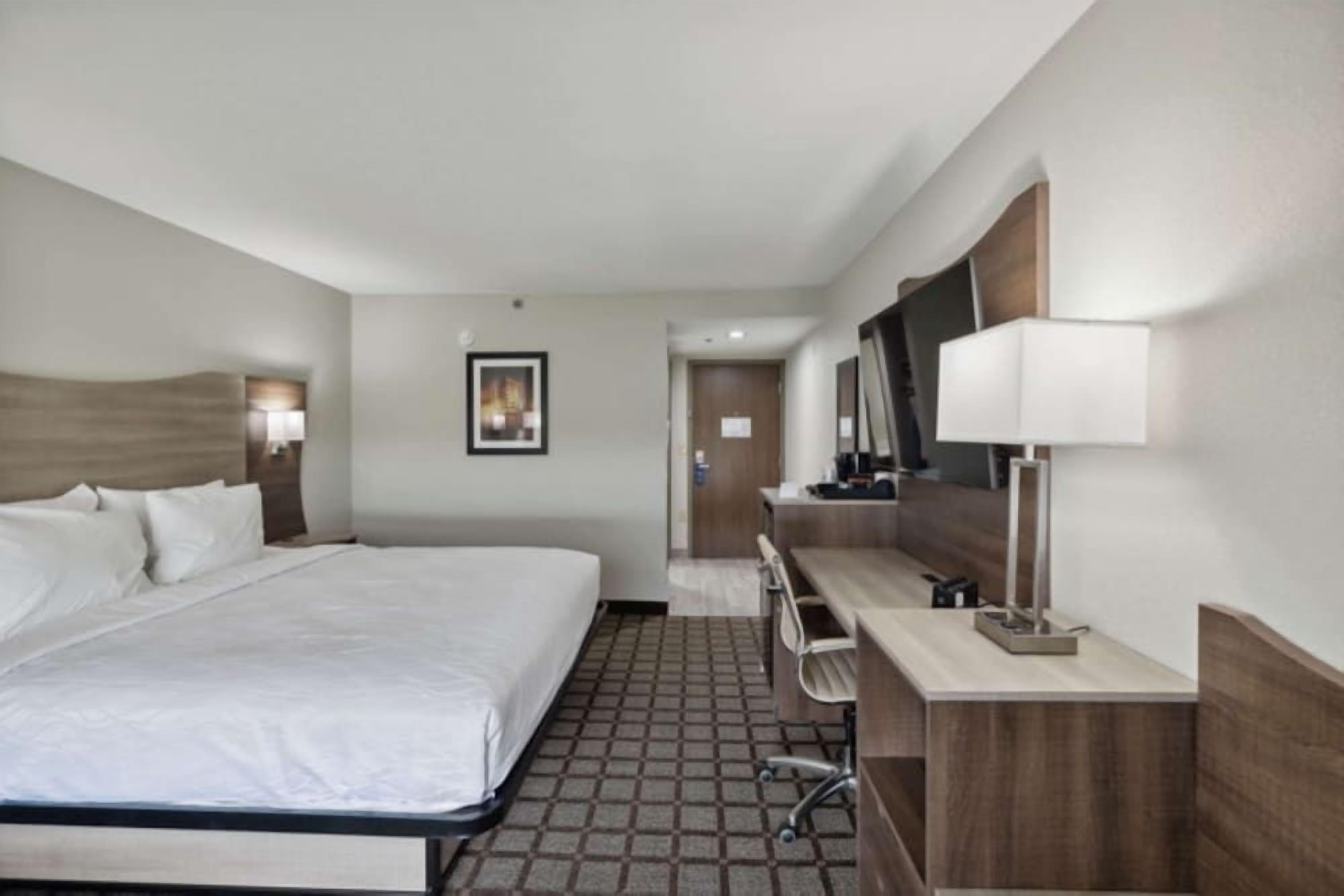 A hotel room with a bed, a desk, a chair, a mirror, and a picture on the wall.