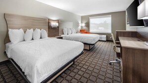 Hotellihuone, jossa on kaksi sänkyä, työpöytä, tuoli, televisio ja ikkuna.
