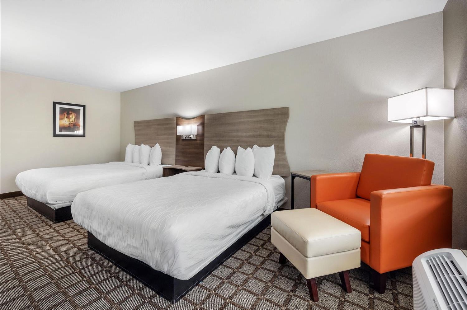 A hotel room with two beds, a nightstand, an orange armchair, a lamp, and a wall-mounted picture.