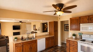 A kitchen with wooden cabinets, a dishwasher, a stove, and a ceiling fan. - Buccaneer Bay #28 - Beachfront Bliss (Sunrise Beach)