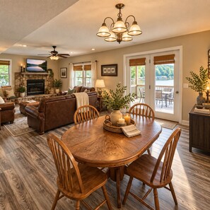 A spacious living room with a fireplace, a dining area with wooden chairs, and a ceiling fan. - Buccaneer Bay Resort Cottage #56 (Sunrise Beach)