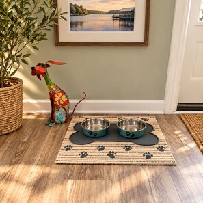 A dog house with a colorful design next to a potted plant and two metal dog bowls on a mat with paw prints. - Buccaneer Bay Resort Cottage #56 (Sunrise Beach)
