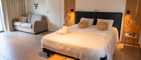 A bedroom with a bed, bedside tables, a small wooden stool, a sofa, and a door.
