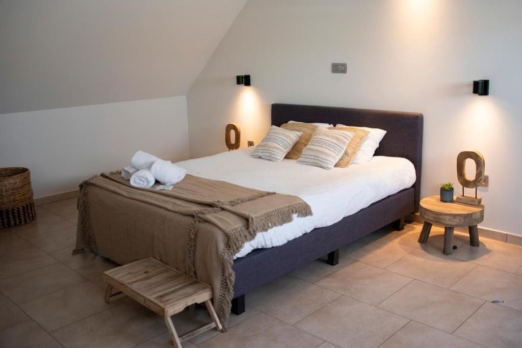 A modern bedroom with a bed, bedside tables, a bench, and wall-mounted lights.