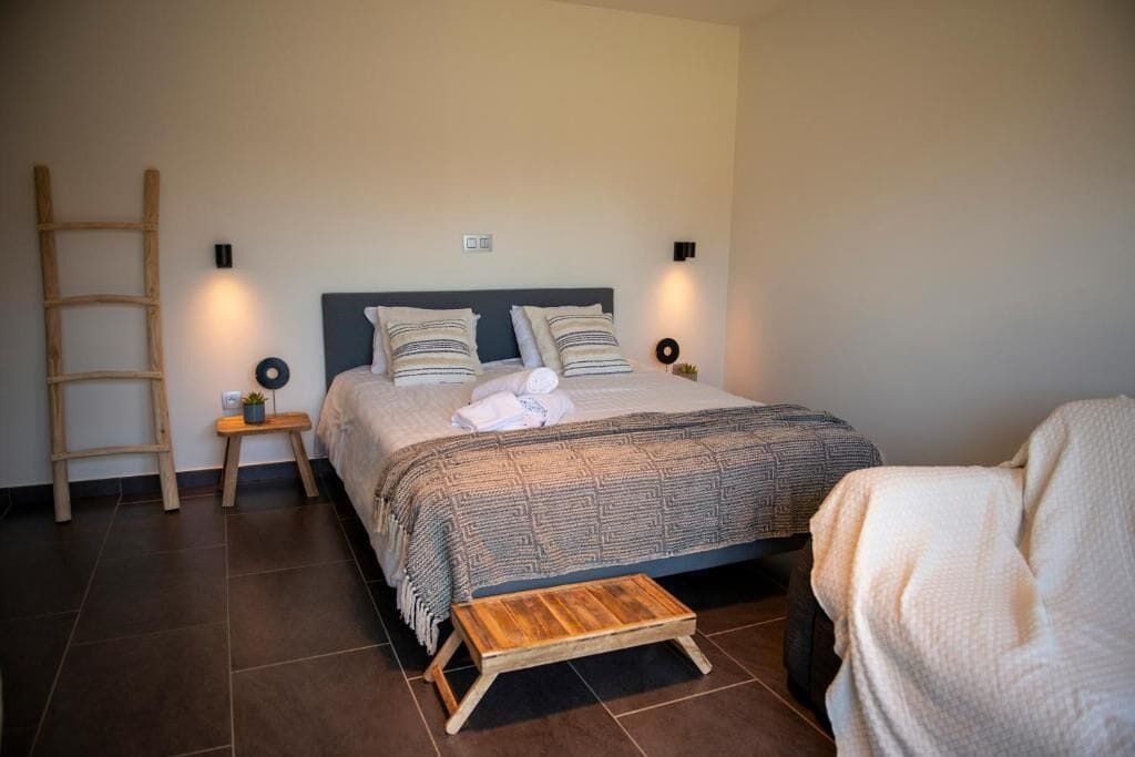 A bedroom with a bed, bedside tables, a wooden ladder, and a small stool.