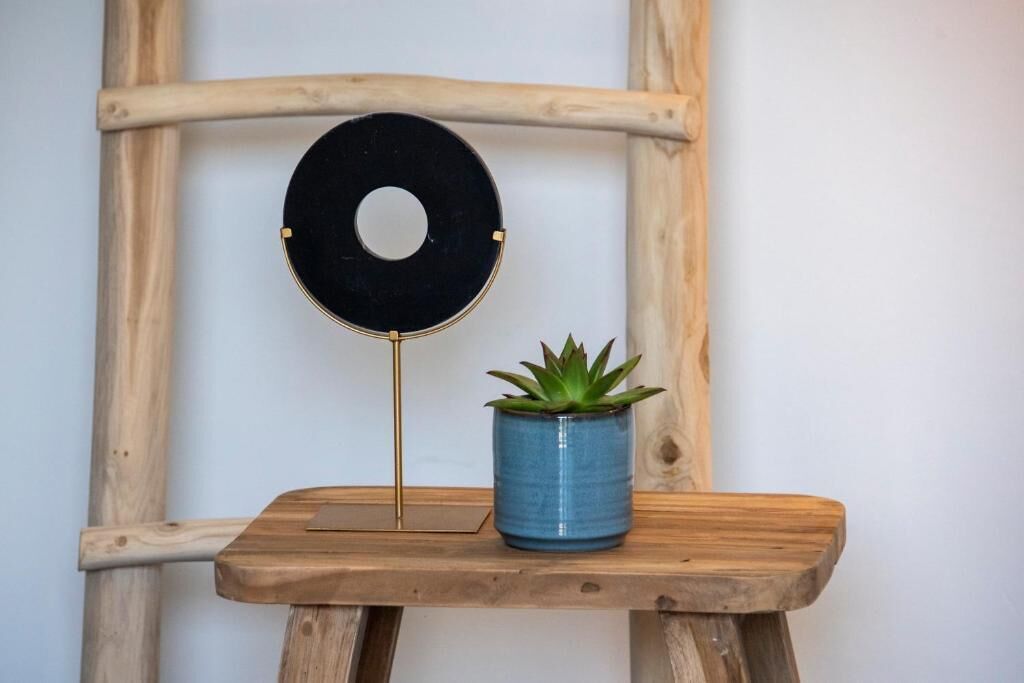 A wooden stool with a blue pot and a black circular object on a stand.