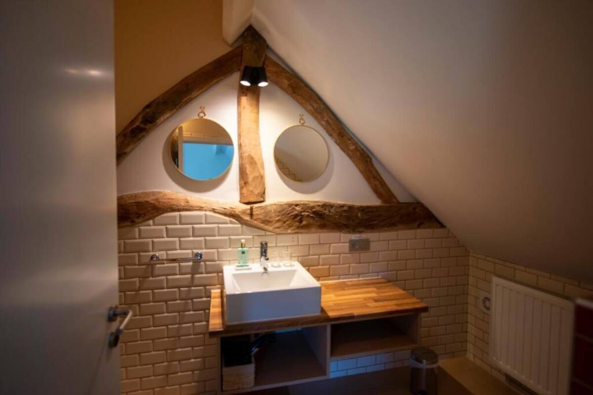 Un baño con lavamanos blanco, tocador de madera, dos espejos redondos y vigas de madera a la vista.
