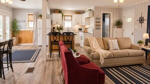A spacious living area with a red sofa, a beige couch, and a dining table with chairs. There are ceiling fans, a kitchen in the background, and a large window with curtains. - Buccaneer Bay Resort 62 (Sunrise Beach)