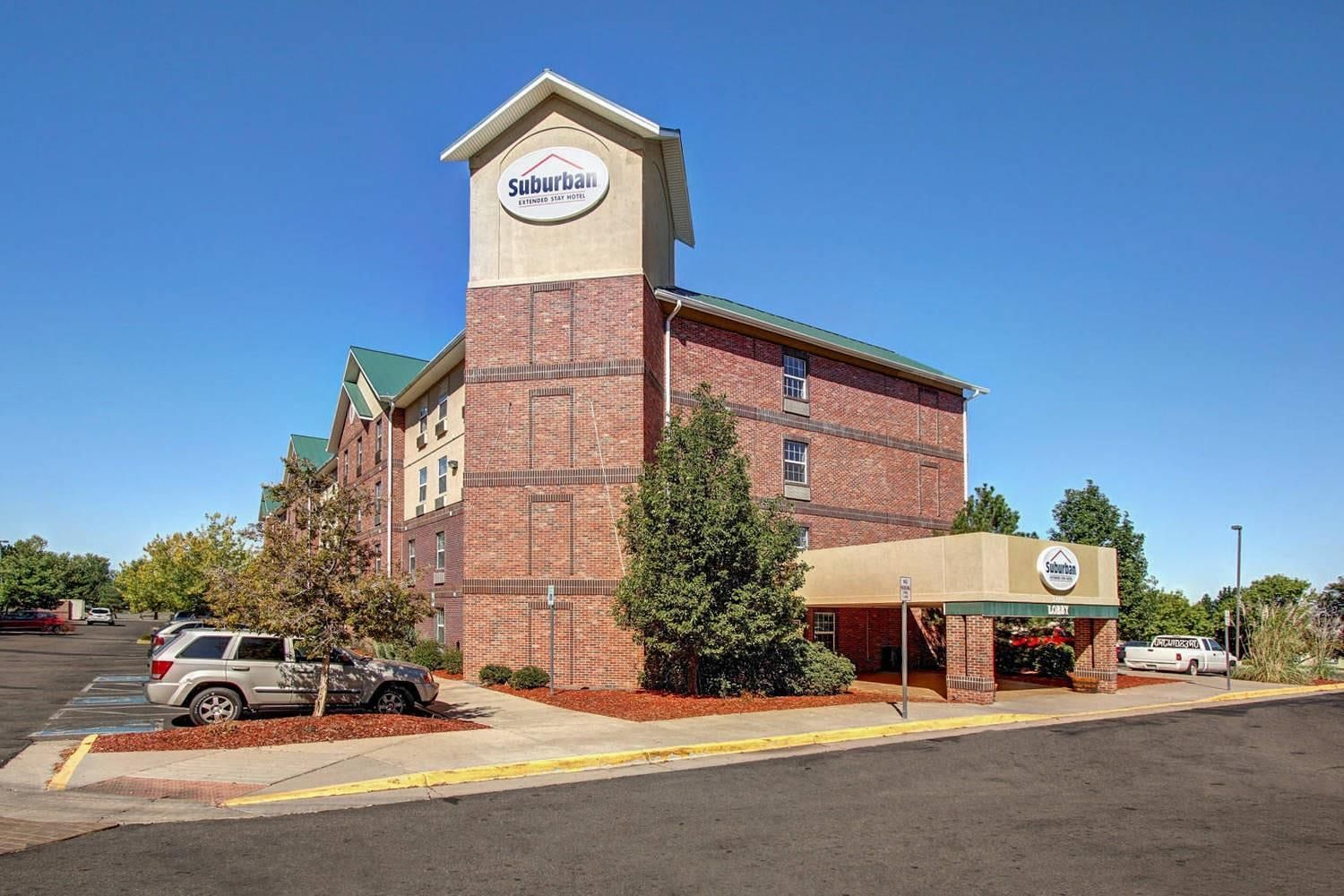 Un hotel para estancias prolongadas en las afueras, con fachada de ladrillo, una torre destacada con el nombre del hotel y un acceso cubierto.