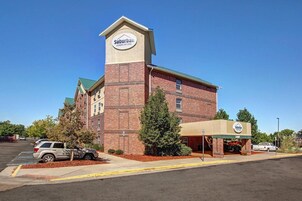 Un hotel para estancias prolongadas en las afueras, con fachada de ladrillo, una torre destacada con el nombre del hotel y un acceso cubierto.