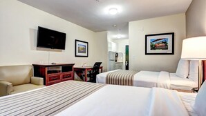 Une chambre d’hôtel avec deux lits, un bureau, une chaise, une télévision et un tableau encadré au mur.