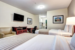 Hotellihuone, jossa on kaksi sänkyä, työpöytä, tuoli, televisio ja seinällä oleva kehystetty kuva.
