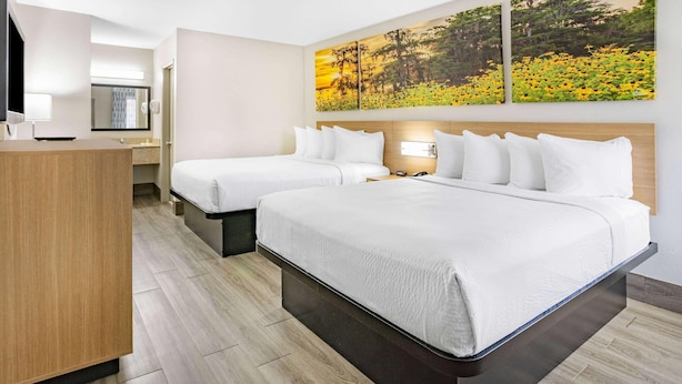 A hotel room with two beds, a wooden desk, a mirror, and two paintings on the wall. - Days Inn by Wyndham Leeds (Leeds)