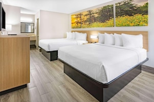Una habitación de hotel con dos camas, un escritorio de madera, un espejo y dos cuadros en la pared.