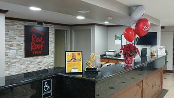 A hotel reception desk with a Red Roof Inn sign, a wheelchair accessibility sign, and a bulletin board with a children's poster.