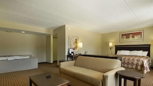A hotel room with a sofa, a small table, a bed with a quilt, a nightstand, a lamp, and a painting on the wall. - Days Inn by Wyndham Leeds (Leeds)