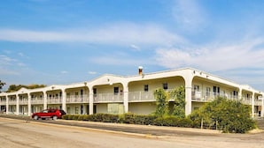 Un motel con varios balcones, un coche rojo estacionado al frente y un cielo azul despejado.