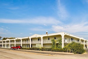 Un motel con varios balcones, un coche rojo estacionado al frente y un cielo azul despejado.