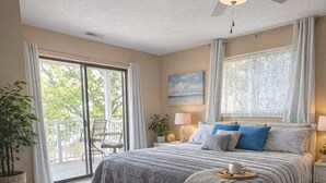 Une chambre à coucher comprenant un lit, un ventilateur de plafond, une fenêtre avec des rideaux, une table de chevet et une commode.
