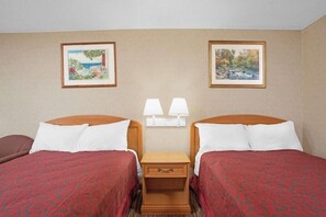 Une chambre d’hôtel avec deux lits, une table de chevet avec des lampes et deux tableaux encadrés au mur.