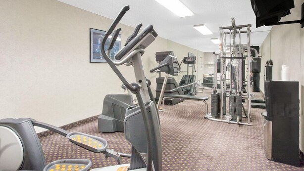 A gym with exercise equipment, a large mirror, and a television. - Days Inn by Wyndham Perryville (Perryville)