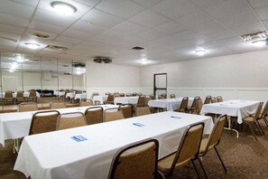 Une salle de conférence dotée de plusieurs tables et chaises, d’un grand miroir et d’un plafond blanc avec des luminaires encastrés.