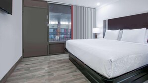 Una habitación de hotel con cama, televisor, ventana con persianas y puerta.