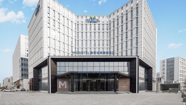 Un microhotel moderno con un llamativo letrero 'MICROHOTEL BY WYNDHAM', fachada de vidrio y un diseño geométrico y limpio.