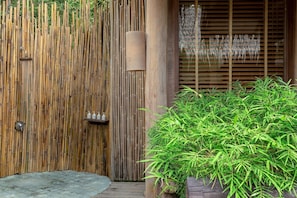 A bamboo wall with a shower, a wooden door, and a potted plant.