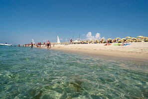 A beach with clear water, umbrellas, and people. - Futura Club Porto Kaleo (Cutro)