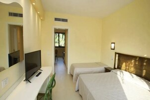 Habitación de hotel con televisor, dos camas, un espejo y vista a un pasillo.