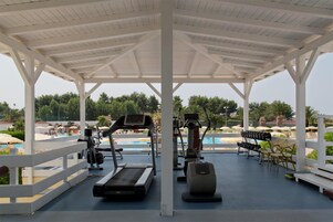 Zona de gimnasio al aire libre con equipo de ejercicio, piscina y sillones de descanso.