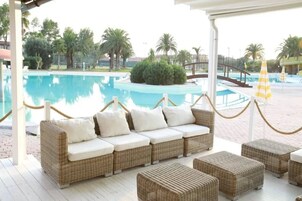 Zona junto a la piscina con mobiliario de mimbre y vista al agua.
