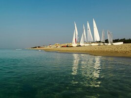 Una playa con veleros alineados en la orilla, agua cristalina y sombrillas.