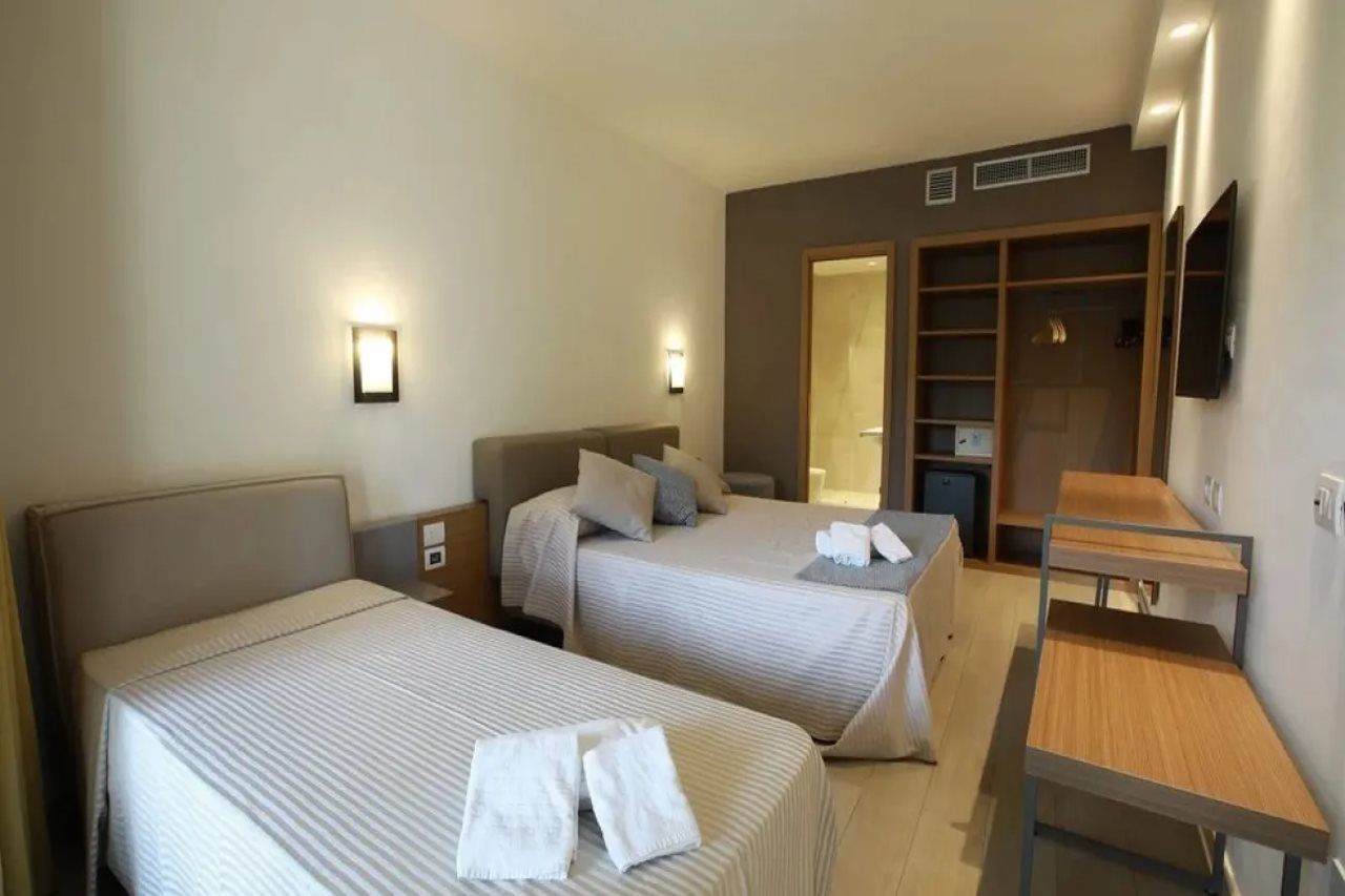 A hotel room with two beds, a desk, and a wardrobe.