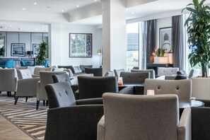 A modern hotel lobby with a mix of seating areas, including sofas and armchairs, a reception desk, and a large window offering a view of the outdoors. - Garner Hotel Preston Samlesbury (Preston)