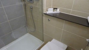 A small bathroom with a shower, toilet, and a shelf with toiletries. - Garner Hotel Preston Samlesbury (Preston)